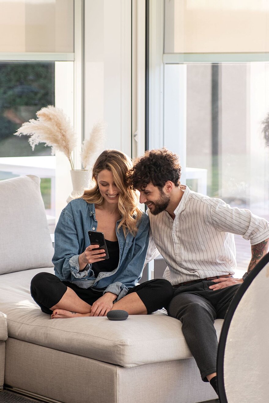 Mann und Frau sitzen auf dem Sofa und schauen ins Smartphone