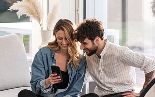 Mann und Frau sitzen auf dem Sofa und schauen ins Smartphone